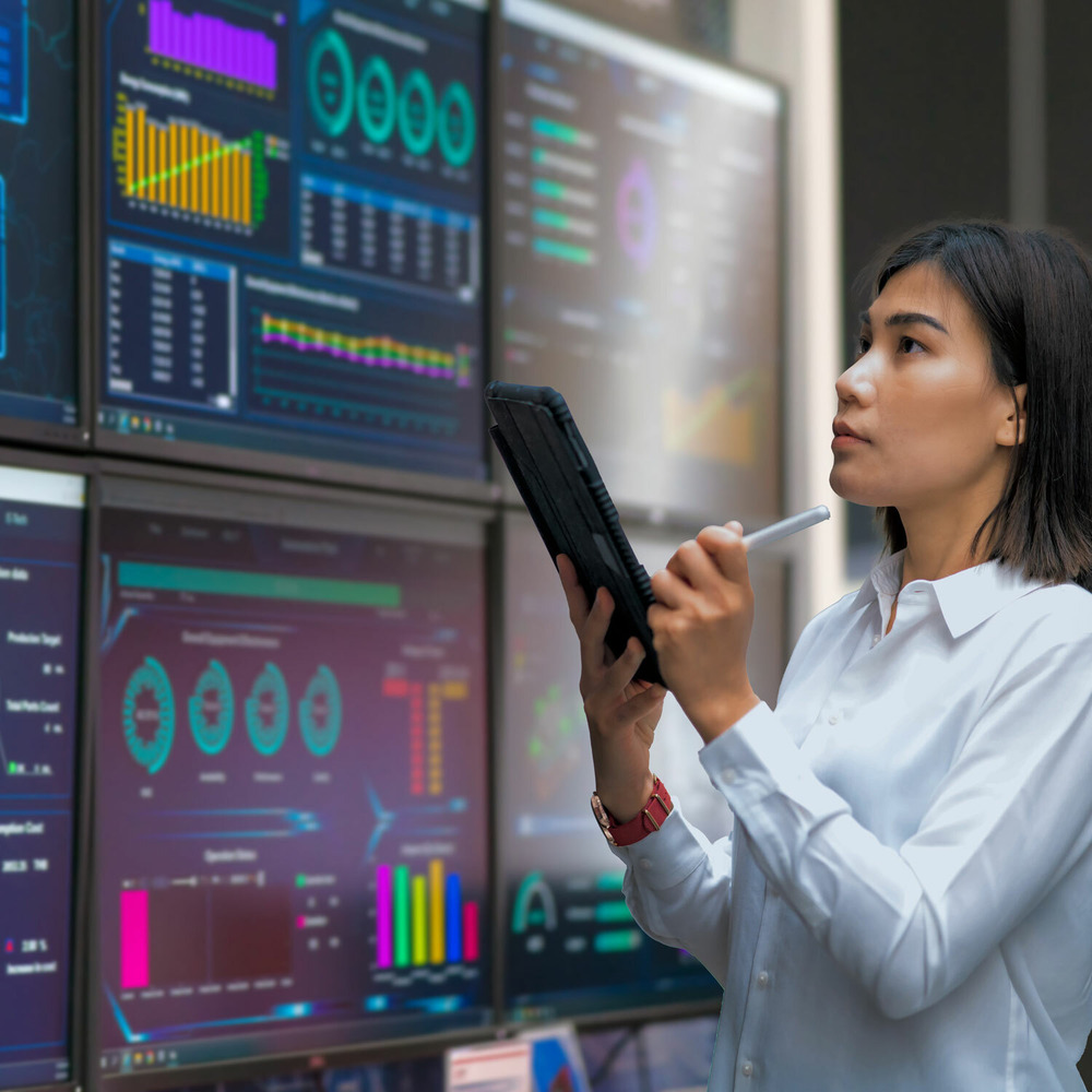 A professional in a white shirt is looking over performance data on multiple screens