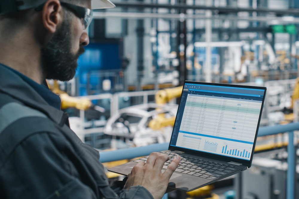 Person working on a laptop overlooking an assembly line