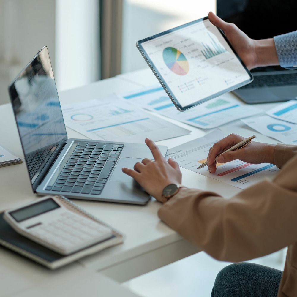 Two marketing professionals sitting at a table with a laptop, tablet, and calculator