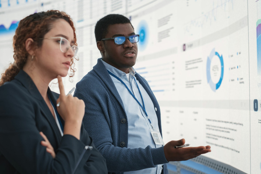 Two marketing professionals speaking in front of a large wall-sized screen