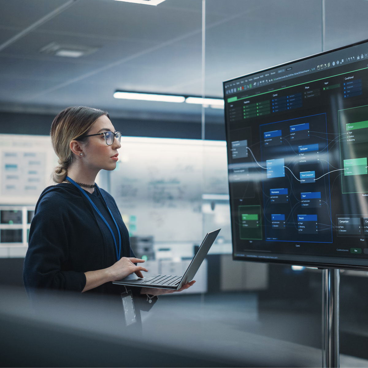 Woman using laptop, analyzing AI-driven insights on a digital screen in a modern office setting.
