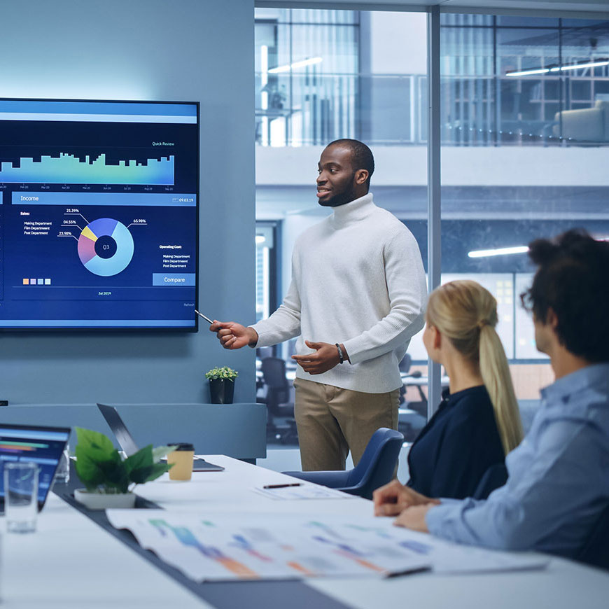 Man presenting analytics on a screen to colleagues in a modern office setting.