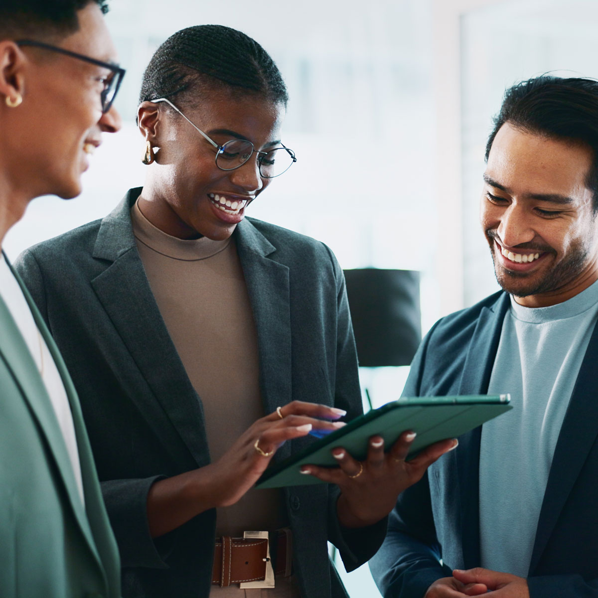 Three colleagues smiling while discussing a project on a tablet during a training session.