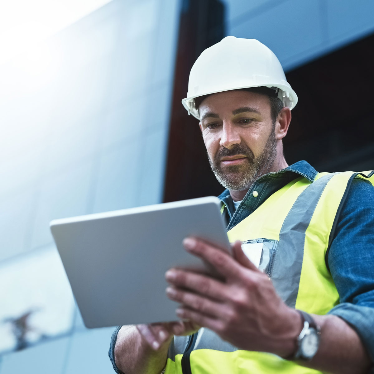 An AEC professional looking at a tablet with a white hard hat and a yellow vest