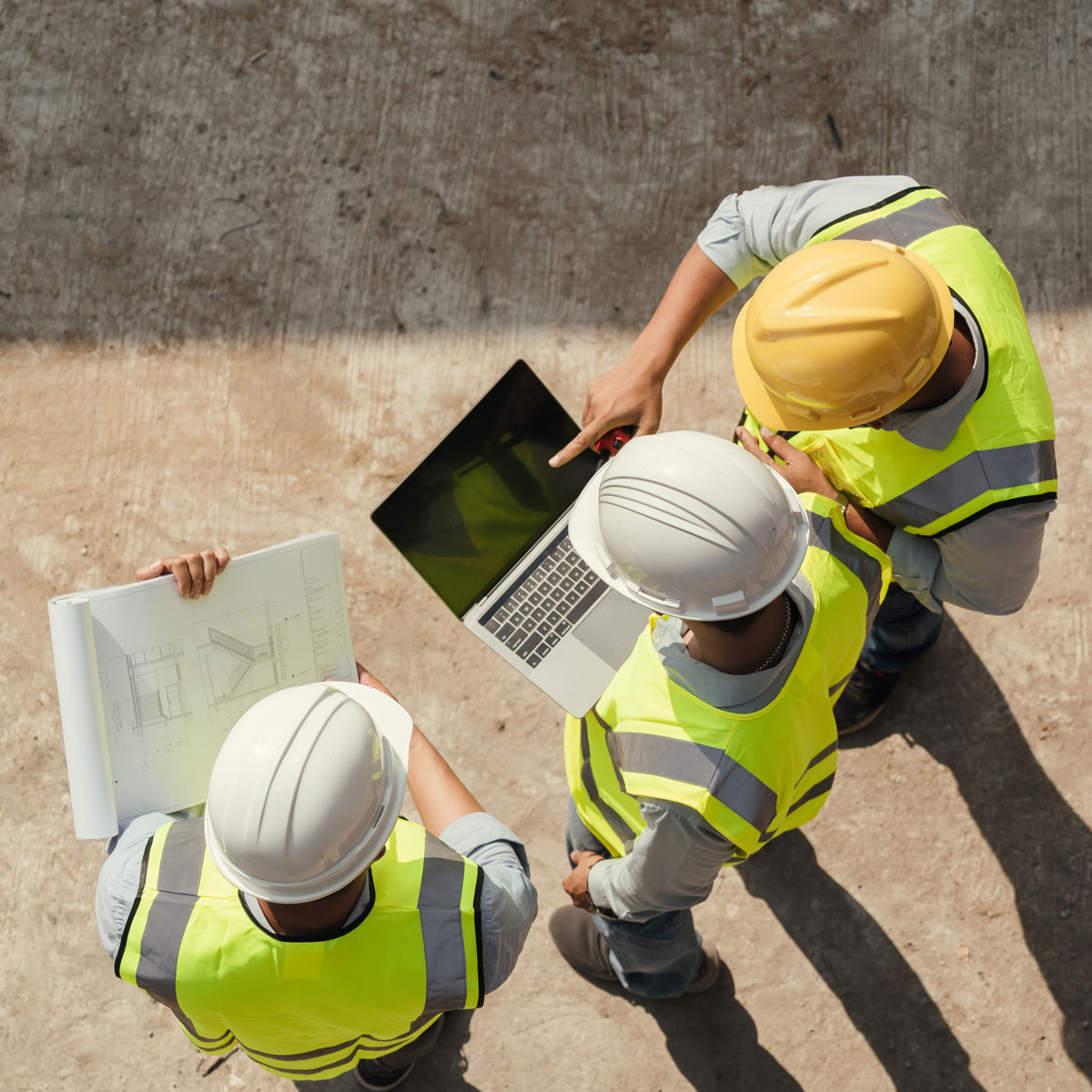 Team of architects, engineers, and construction professionals at a job site looking over a laptop