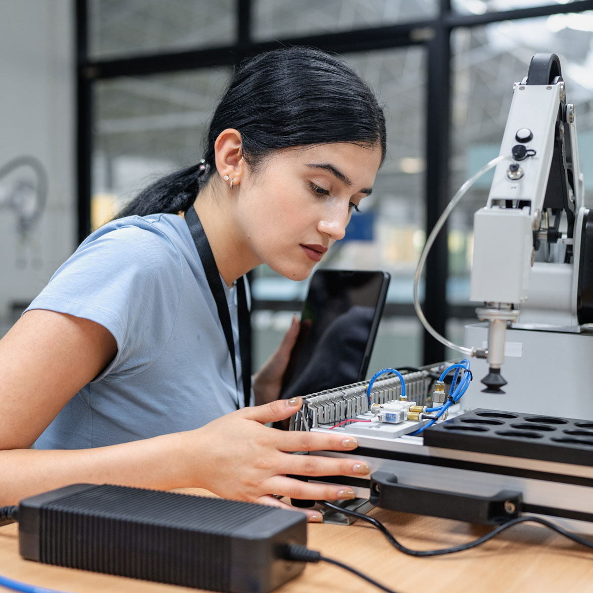 Young woman in blue shirt working with robotic equipment and tablet in tech lab, demonstrating focus and innovation.