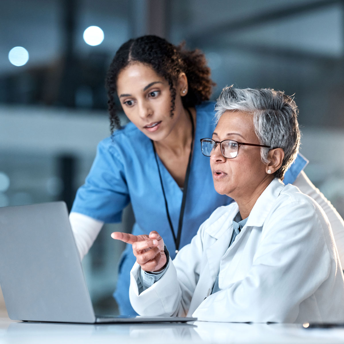Medical professionals collaborate at a laptop; doctor and nurse discussing patient care in a hospital setting.